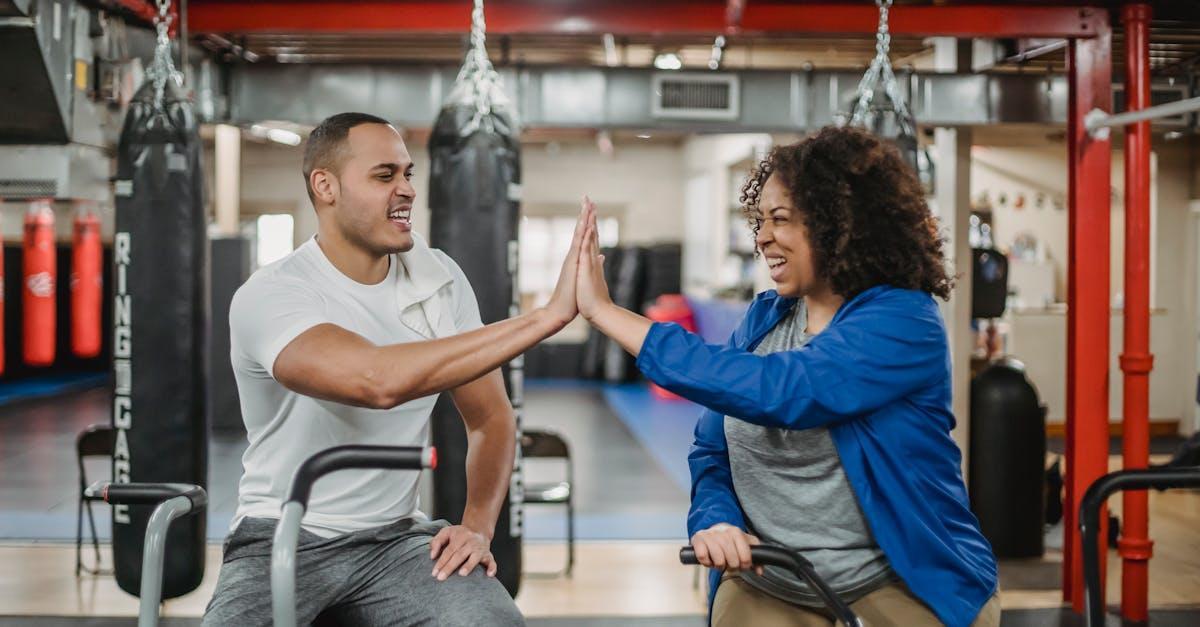 Cheerful plump African American female trainee and fit smiling male coach clapping each others hands while training in spacious equipped gym