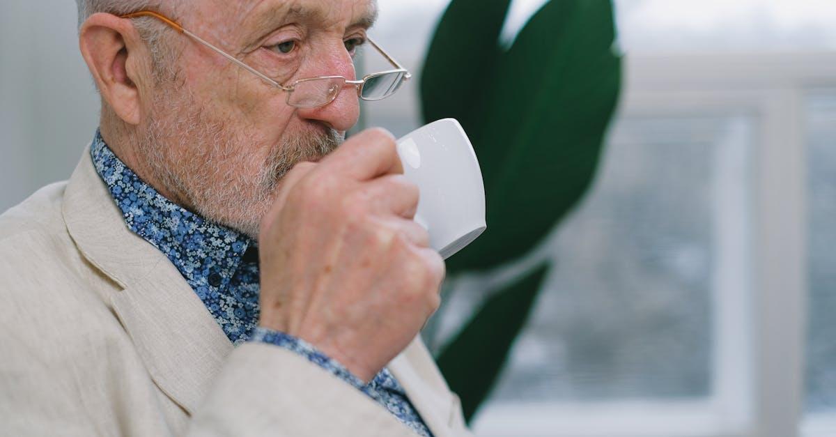 Senior man with eyeglasses enjoying a coffee indoors, conveying a sense of leisure and tranquility.